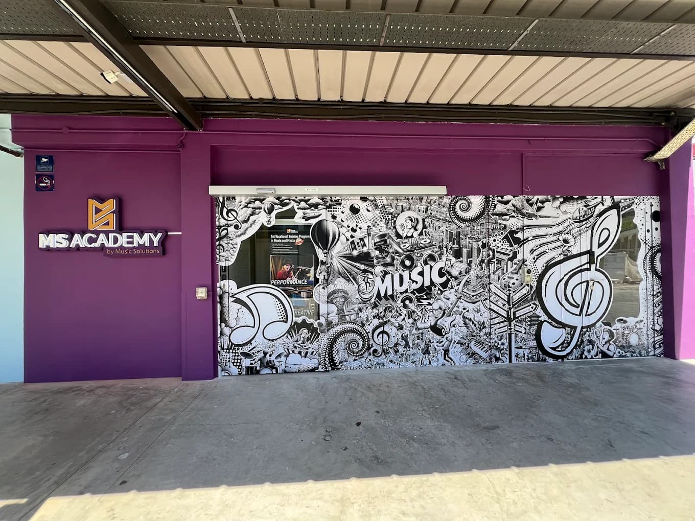 MS Academy shopfront exterior with a purple facade, illuminated MS Academy signage and a black-and-white music-themed mural