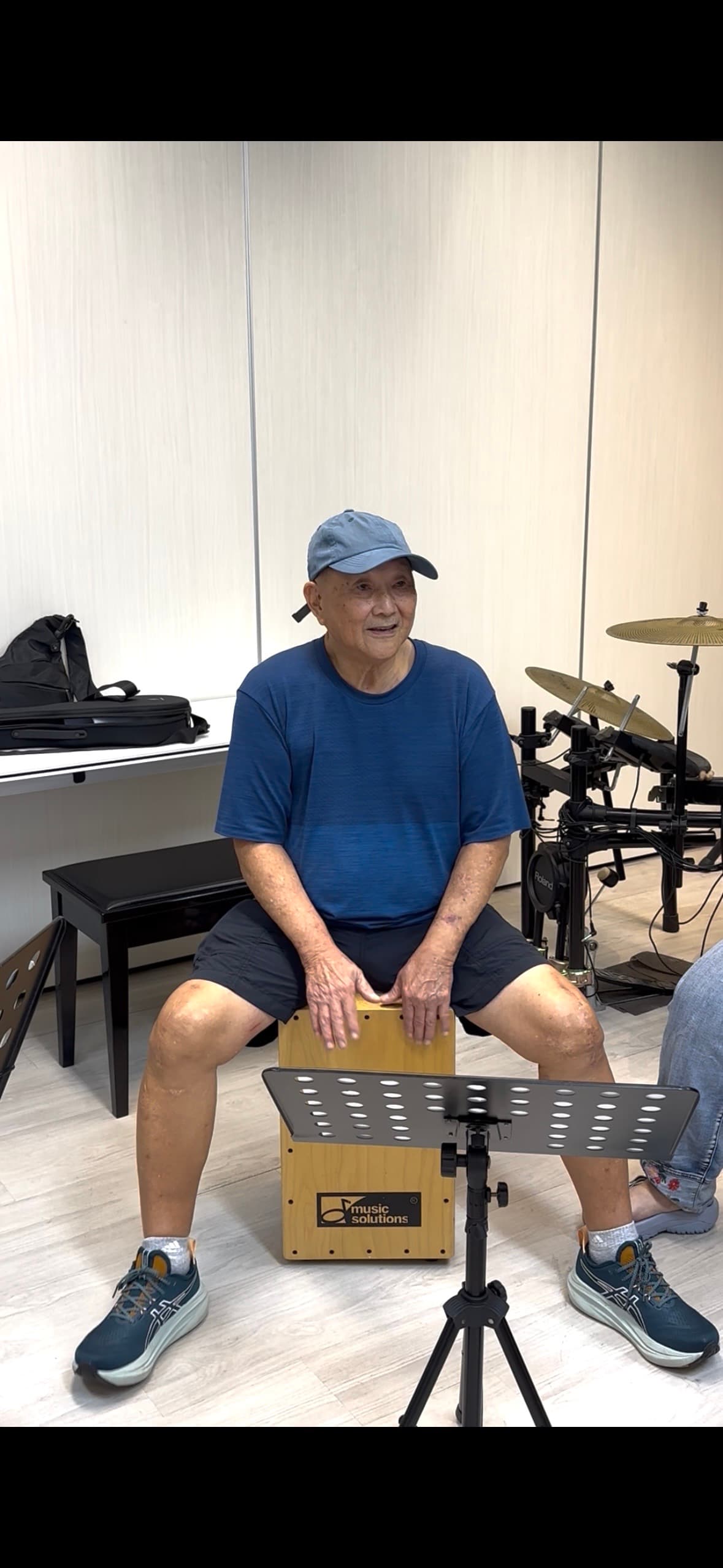 A learner playing a drum kit with a trainer keeping time alongside