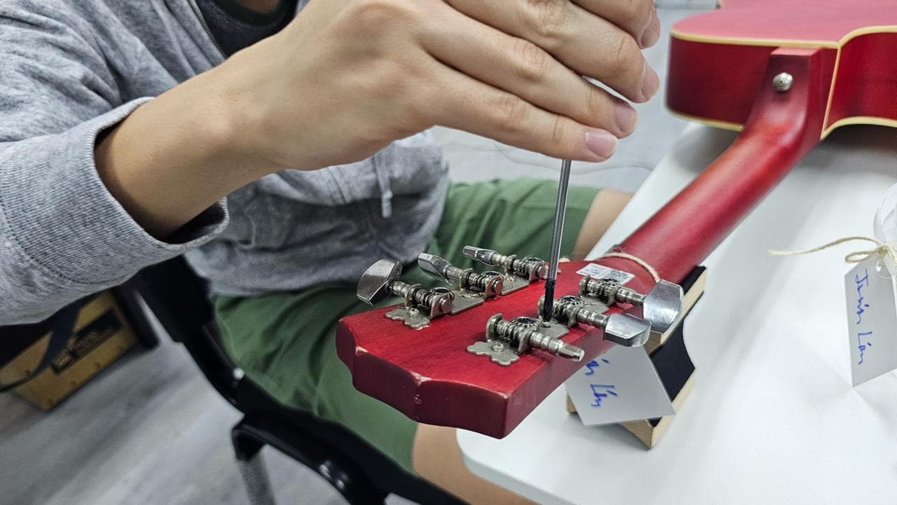 A learner adjusting the tuning machines on the headstock of a red guitar with a screwdriver