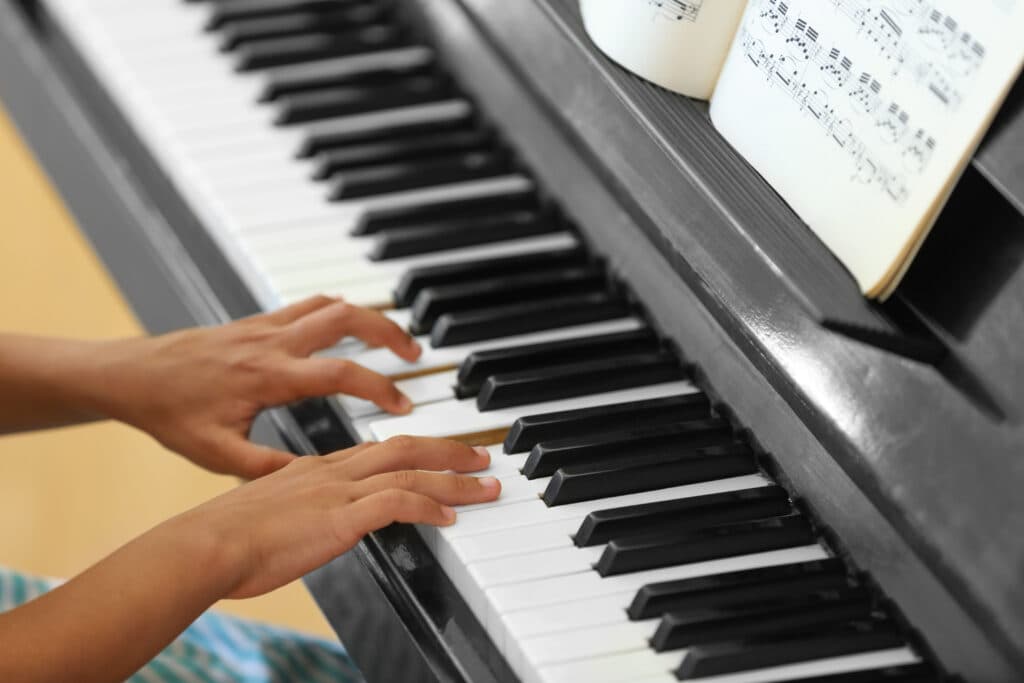 Hands playing melodies at the piano keys with sheet music on the stand
